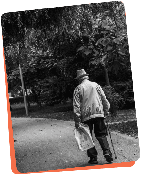 black and white photo of an elderly man walking down a pebble path holding a cane.